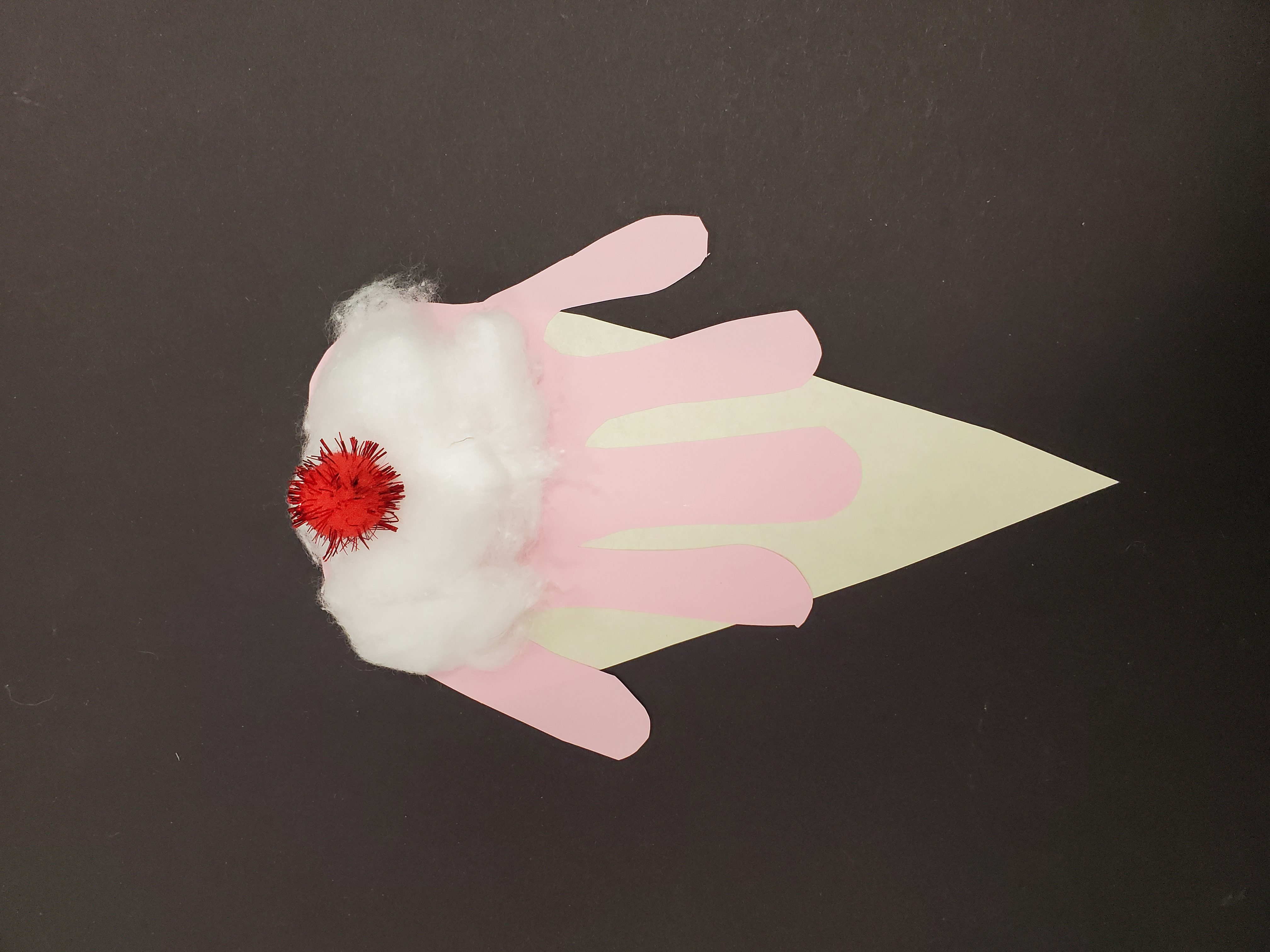 Image of a colorful children's craft made to look like an ice cream cone with whipped cream and a cherry on top. The ice cream portion is made of a pink paper cutout of a child-size handprint.