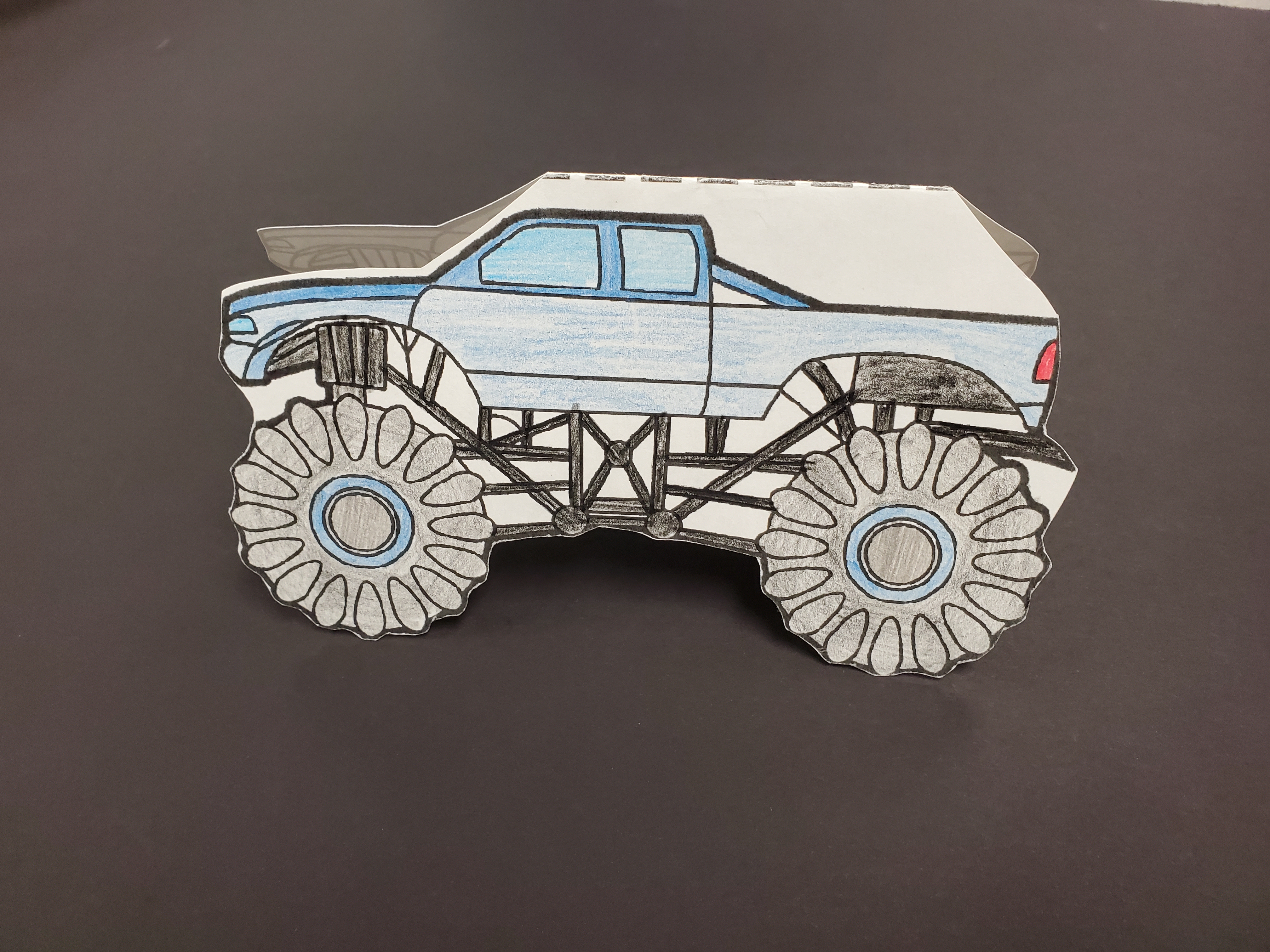 photo of a paper cutout of a monster truck, colored blue and black with crayons