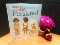 Spotty pops out of a copy of "She Persisted" by Chelsea Clinton