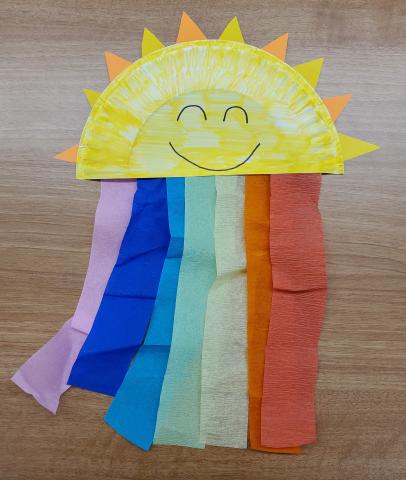 Photo of a Sun & Rainbow craft. The Sun is made from a half paper plate, and the rainbow is colorful streamers hanging from the plate.