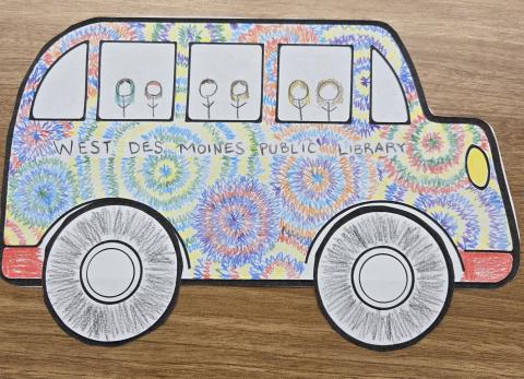 Photo of a paper school bus with rainbow coloring and tiny stick figure people in the windows.