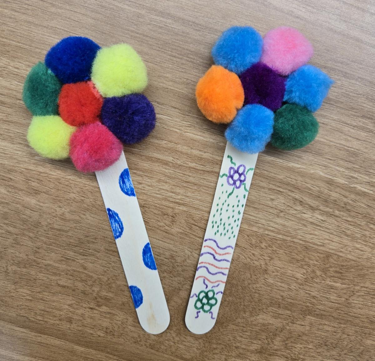 Photo of two pom pom bookmark crafts on a brown table background.