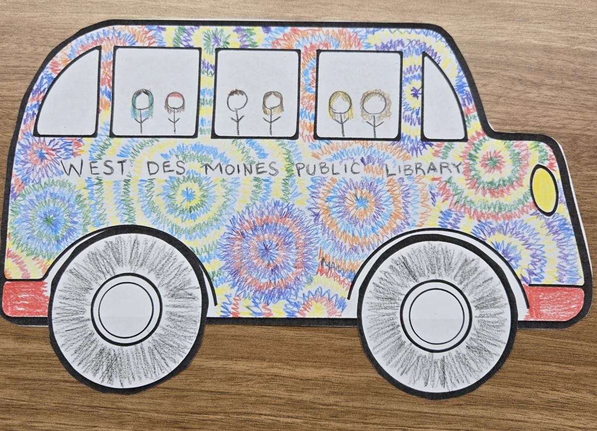 Photo of a paper school bus with rainbow coloring and tiny stick figure people in the windows.